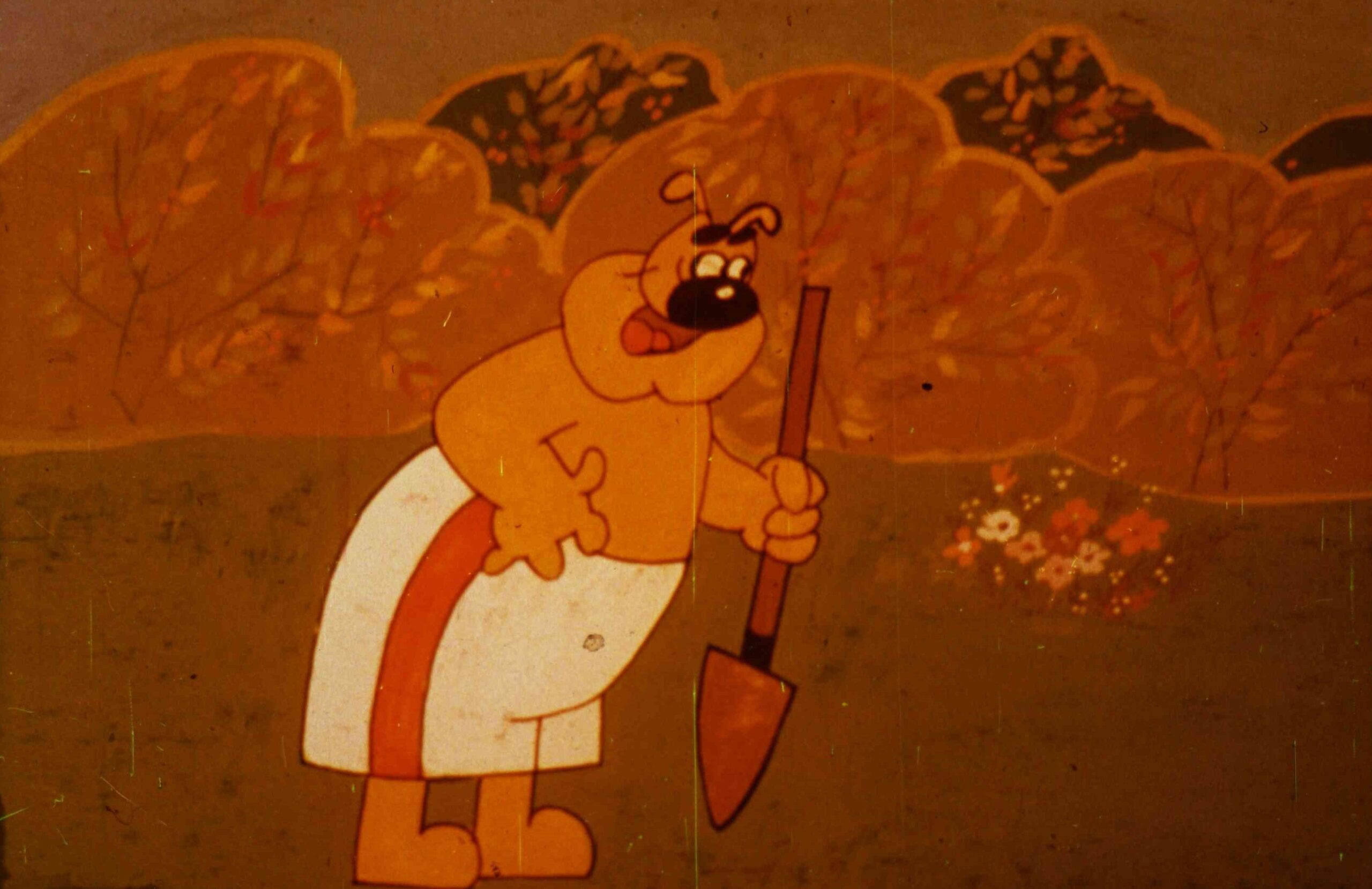 Personaj animat exprimându-se într-un peisaj cu vegetație la care ține o unealtă de grădinărit.