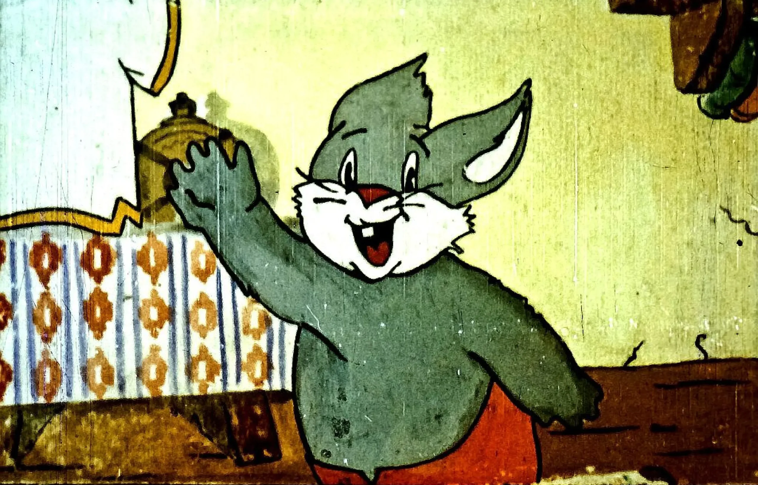 Un personaj animat cu blană gri și urechi mari zâmbește și salută.