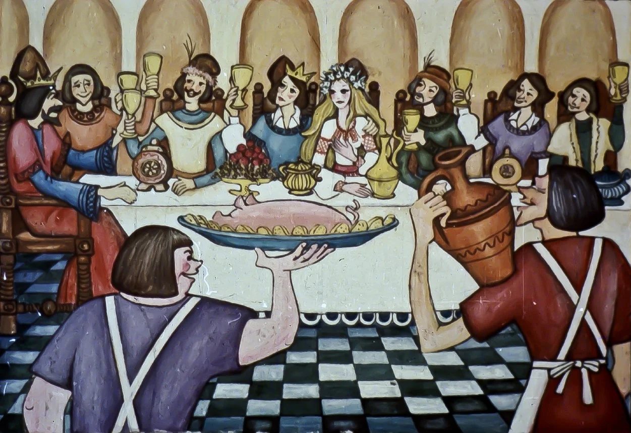 Imaginea ilustrează o nuntă medievală, cu o masă plină de mâncare și băuturi, iar invitații se bucură de festin.