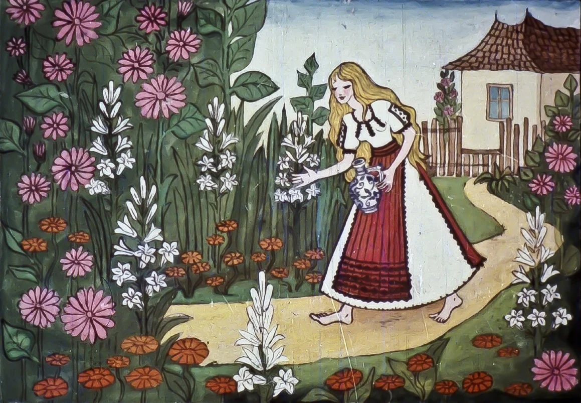O fată îmbrăcată în costume populare merge pe un drum înconjurat de flori, ținând în brațe o floare, cu o casă în fundal.