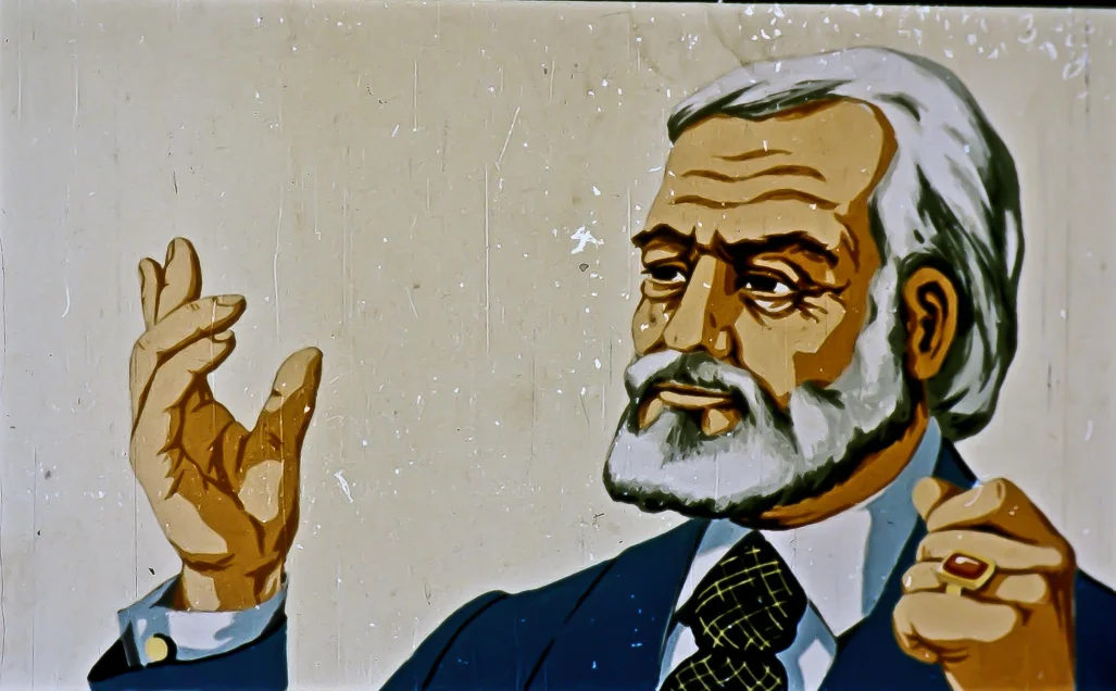 Ilustrație a unui bărbat cu păr alb și barbă, îmbrăcat într-un costum, gesticulând cu o mână ridicată.