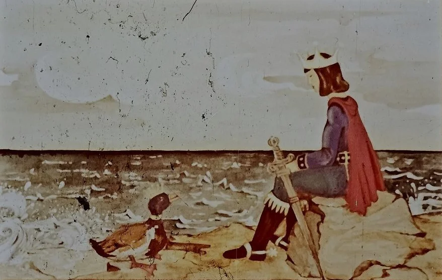 Imagine cu un rege așezat pe o stâncă, privind spre mare, în timp ce un raț se află lângă el.