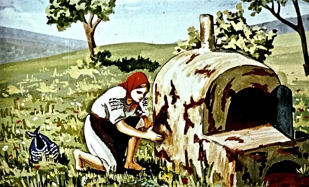 O femeie îngrijind un cuptor dărâpinat într-un peisaj rural.