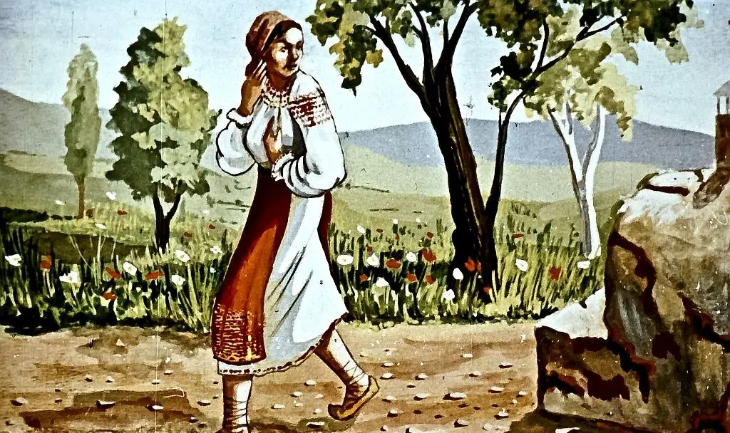 O femeie îmbrăcată în costum popular, mergând pe o alee în natură, cu un peisaj de copaci și munți în fundal.